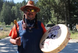 Huu-ay-aht speaker Wišqii drums after the logo was unveiled.