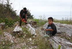 Carson sits on the Northwest coast of Nootka Island, as his father Brandon John operates a chainsaw on June 28. 