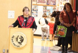 Cloy-e-iis (Dr. Judith Sayers) give a speech at the 50-year milestone event as her daughter Alana watches on in the background.