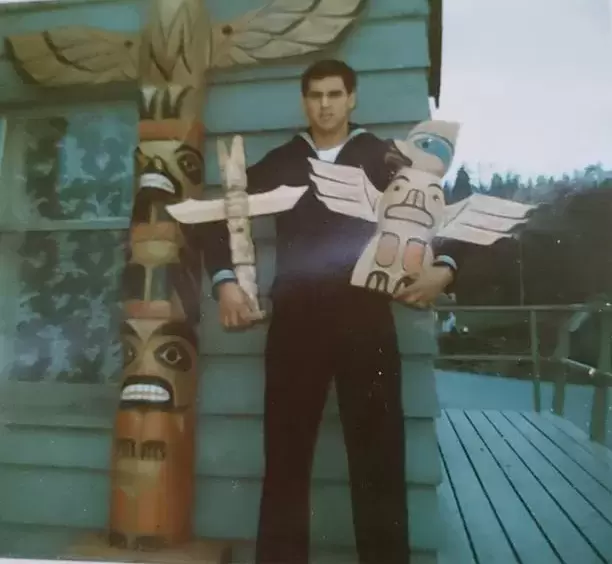 Henry Vincent Thomas, Tseshaht, holding two carvings made by his late father, Henry Thomas Sr., on his house porch in Neah Bay, Washington. Thomas saw active duty in the United States navy 1972-76.