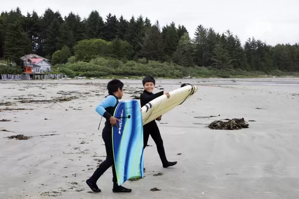 Payton Williams (left) and Ali Swan walk towards the ocean in front of Esowista for surf club, near Tofino, on June 14, 2021.