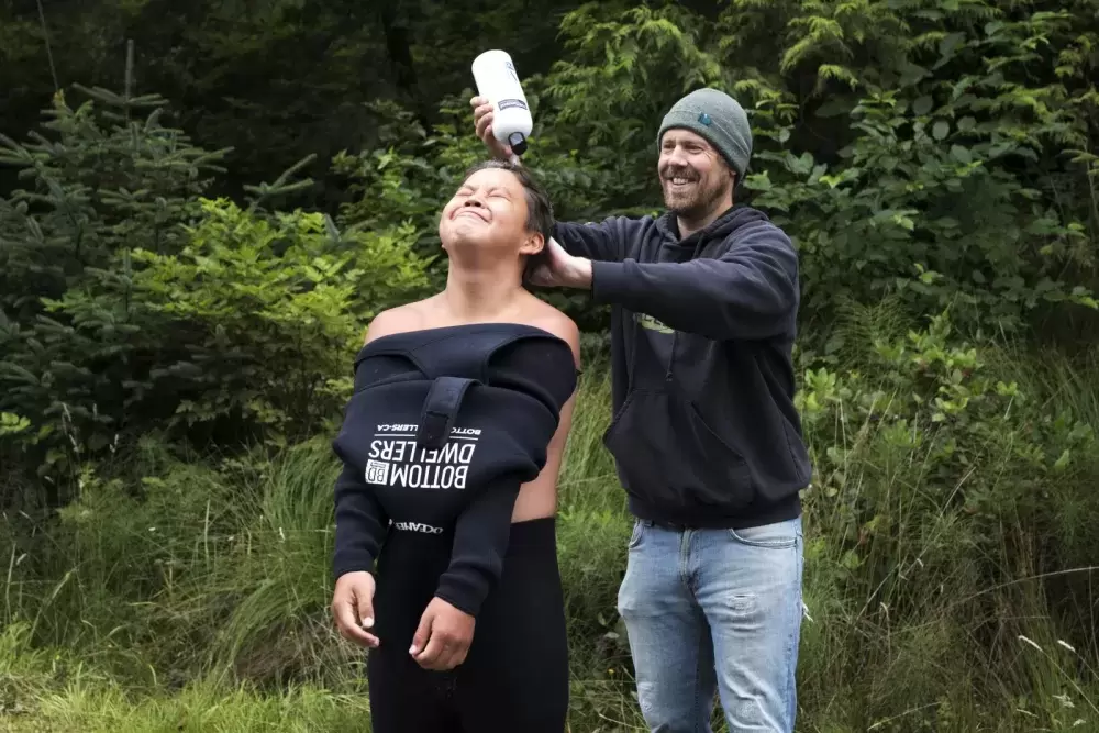Chris Adair, owner of Bottom Dwellers Freediving, pours soap on Kenneth Lucas' head so his wetsuit is easier to pull on, in Ucluelet, on August 18, 2021.