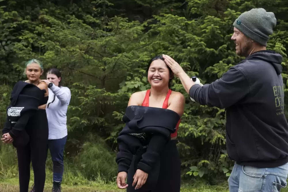 Chris Adair, owner of Bottom Dwellers Freediving, pours soap on Brandi Lucas' head so her wetsuit is easier to pull on, in Ucluelet, on August 18, 2021.